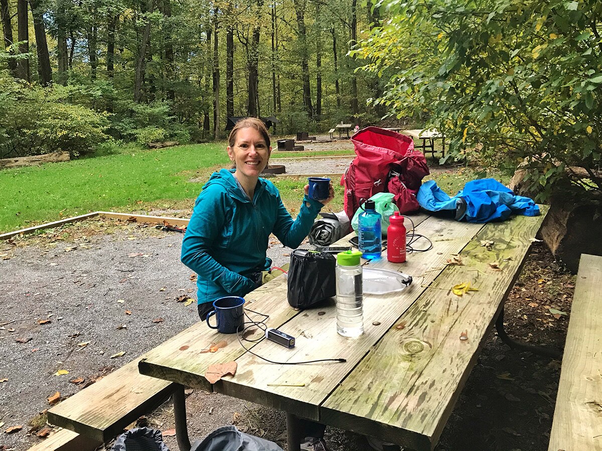 Dr. Mary Evans sitting at a picnic table outdoors with camping gear.