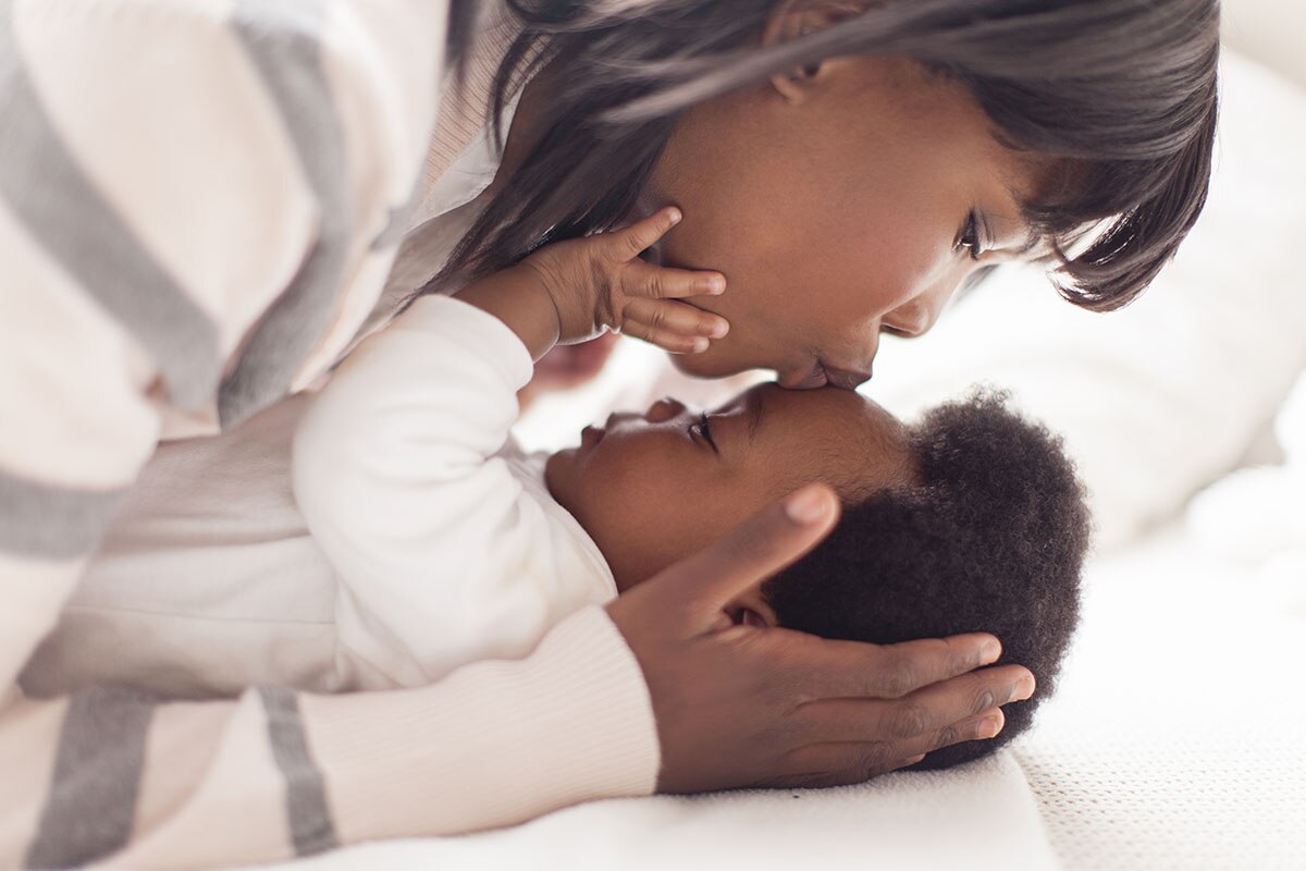  A woman kissing her baby on the forehead.