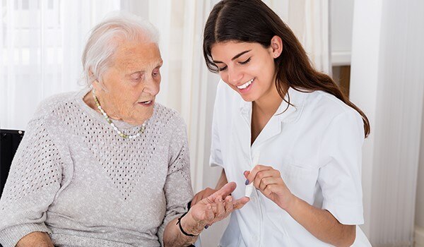A health care professional helping an elderly woman check her blood glucose level.