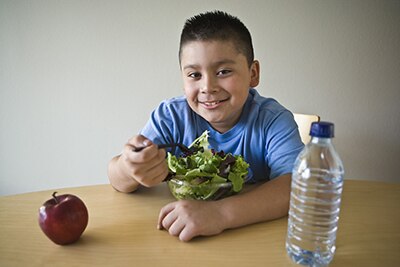 Niño con sobrepeso frente a un tazón de frutas.