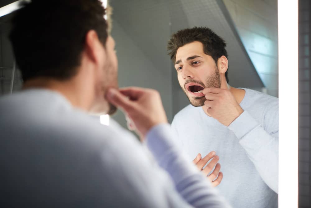 A man checking the inside of his mouth in the bathroom mirror for signs of problems from diabetes.