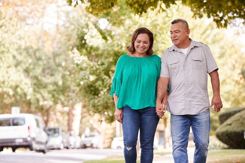 Senior couple walking along suburban street holding hands.