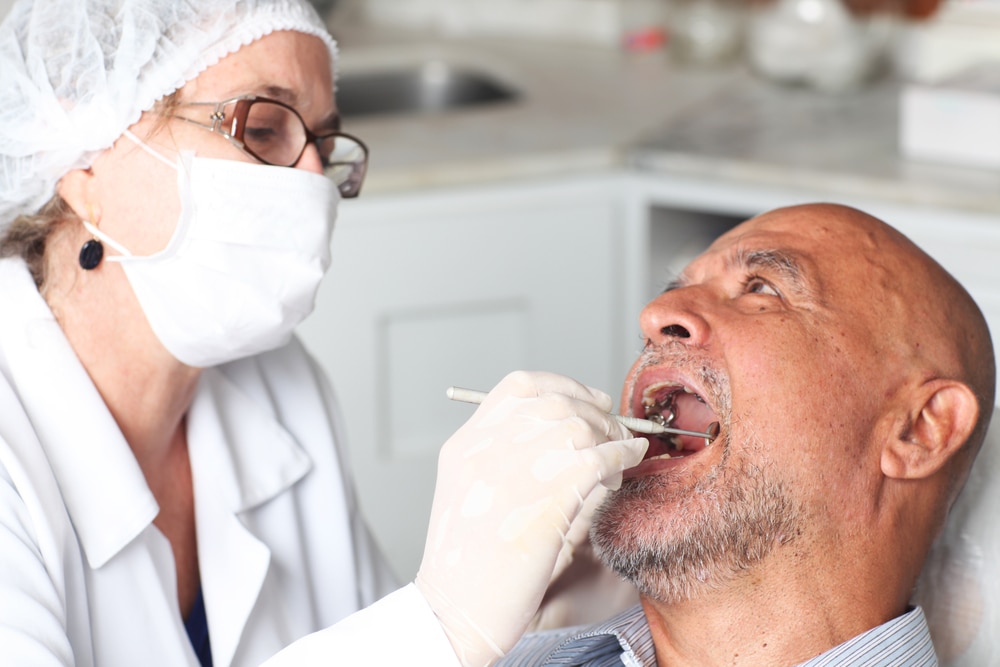 A dental professional examines an older patient’s mouth and teeth using dental tools.