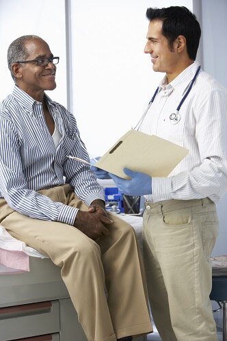 A doctor talking with a male patient who is seated on an examination table.