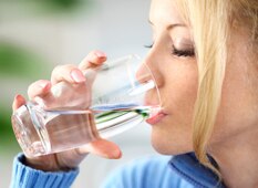 White woman with blonde hair drinking a glass of water.