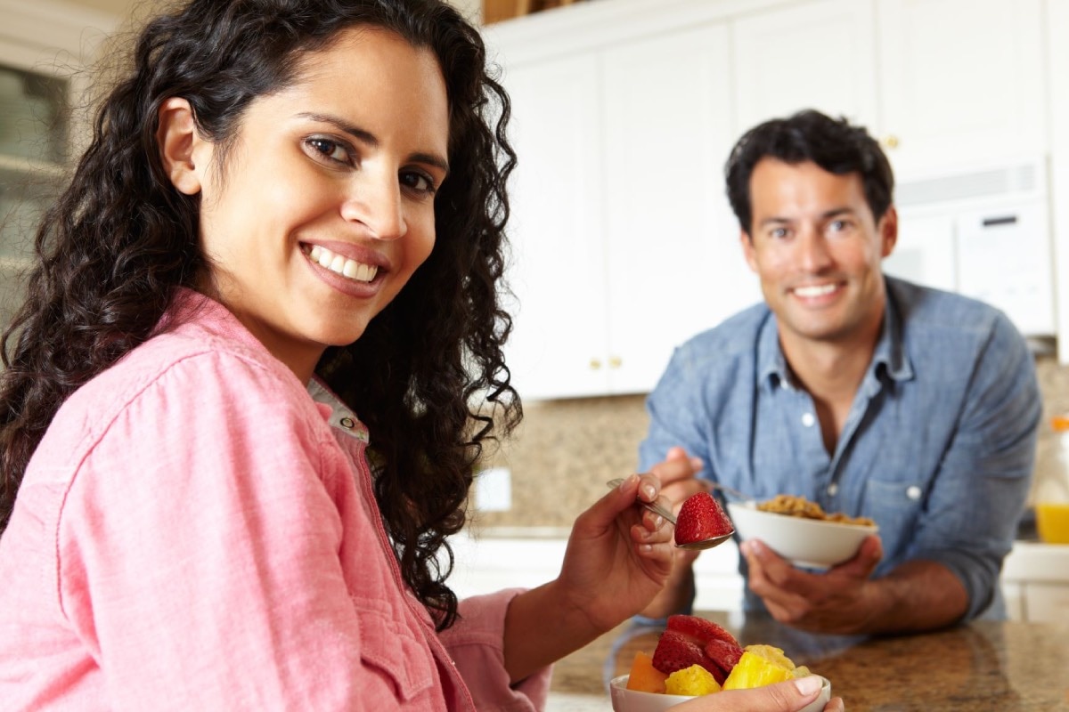 Woman eating small bowl of fruit and man eating small bowl of cereal.