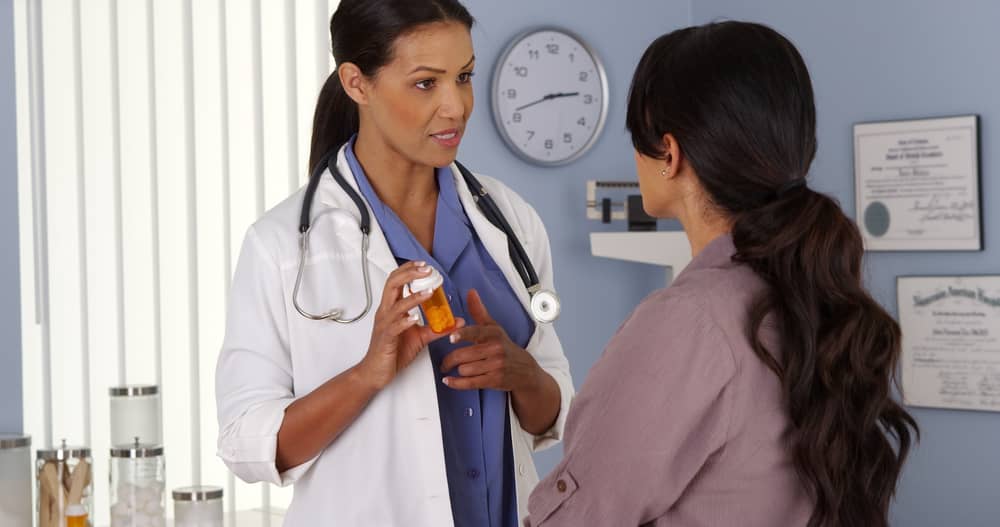 Un médico habla con una paciente mientras sostiene un frasco de prescripción.
