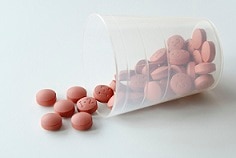Clear cup of nonsteroidal anti-inflammatory drugs (NSAIDs) spilling out onto a table.