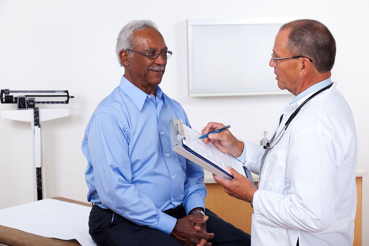 Un profesional de la salud habla con un paciente masculino mientras revisa sus registros médicos.