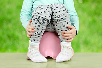 A toddler’s legs are seen as the child sits on a small potty.