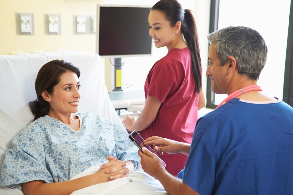 Two health care professionals talking with a patient in a hospital room.