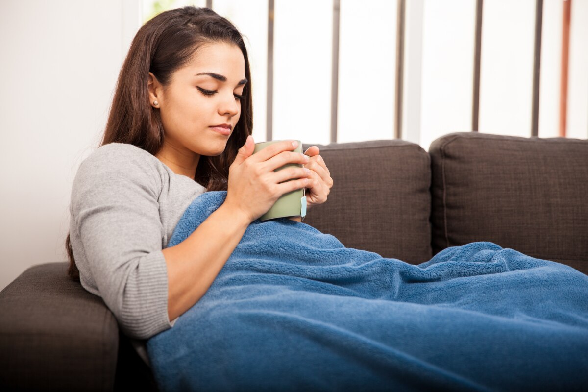 Woman under a blanket with a mug.