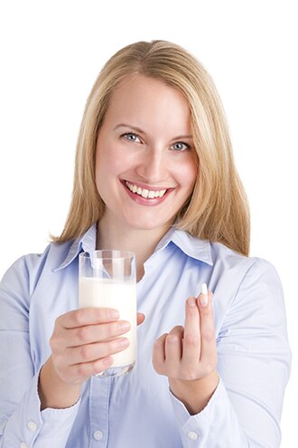 Woman holding a glass of milk and a lactase tablet.