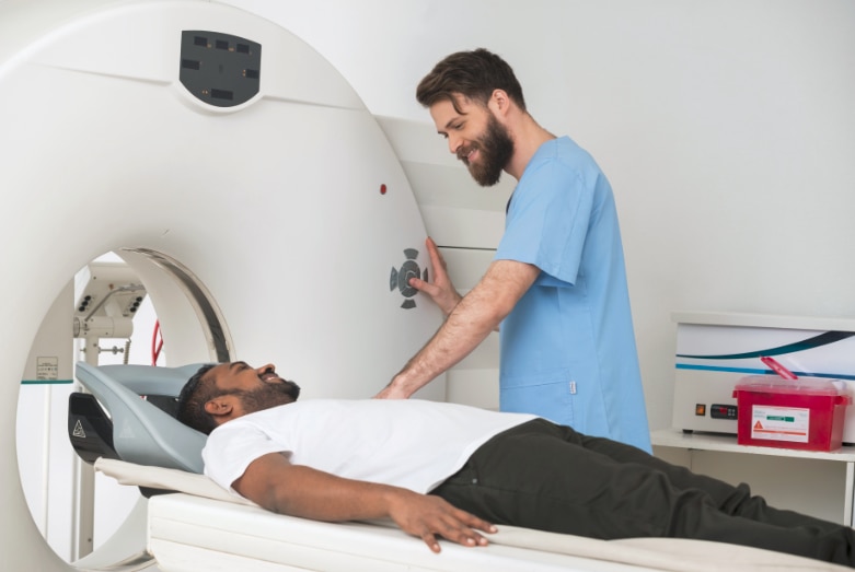 A man lying on a table ready to slide into a doughnut-shaped CT machine with a health care professional by his side.