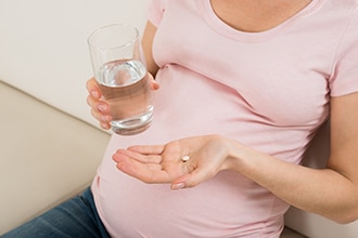 Mujer embarazada con una pastilla en una mano y un vaso con agua en la otra.