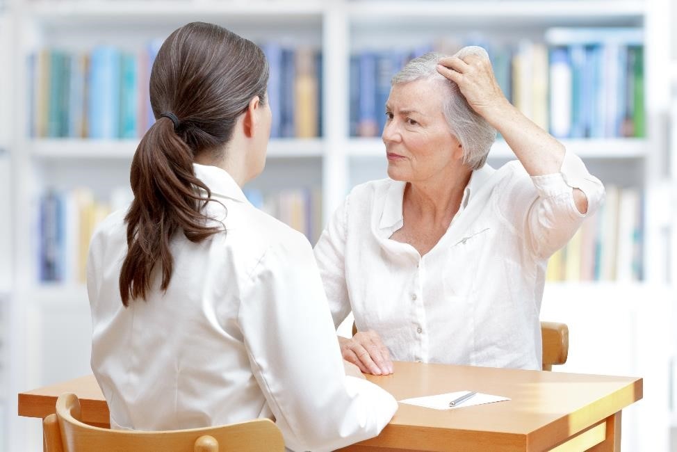 Older woman with gray hair showing her thinning hair to female doctor.