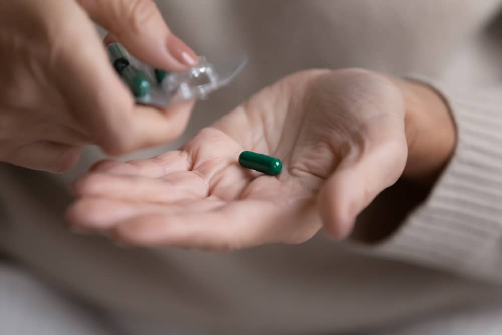 Close-up of a middle-aged woman’s hands pouring a capsule pill out of a plastic blister.