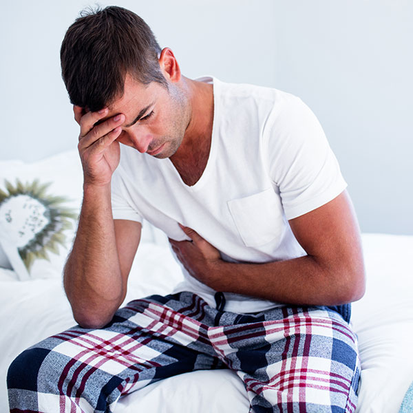 Young man sitting with stomach pain on bed in bedroom