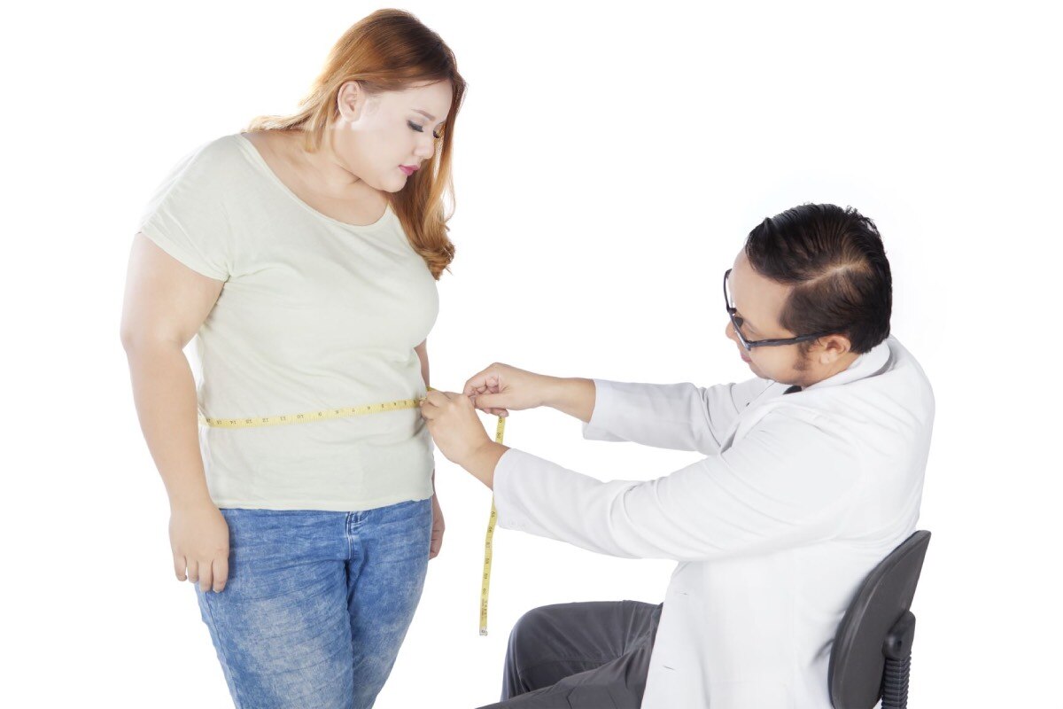 Un médico midiendo la cintura de una mujer.