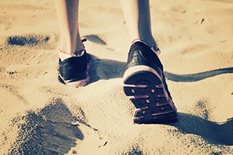 Una persona con zapatos deportivos camina en la arena.