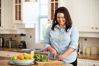 Una mujer joven sonríe mientras corta verduras en su cocina.