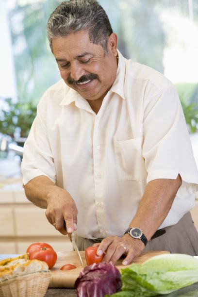 An older male slices up vegetables as he prepares a meal.