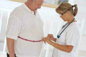 Profesional de la salud midiendo la cintura de un hombre obeso.