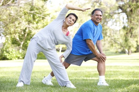 Older man and woman in exercise clothes stretching in a park.