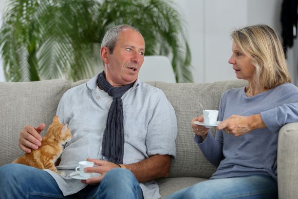 Un hombre mayor habla con su compañera mientras están sentados juntos en un sofá.