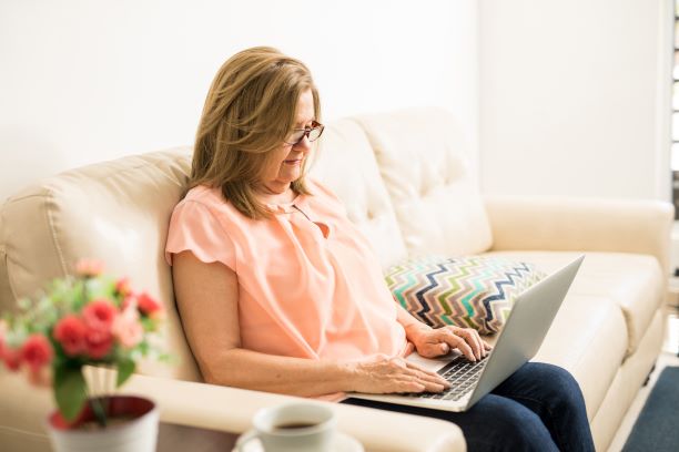 Una mujer usa su computadora portátil mientras está sentada en un sofá.