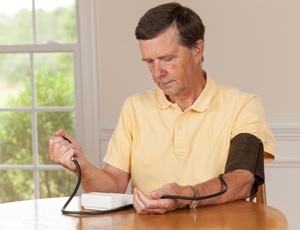 A photo of an older man checking his blood pressure at home.