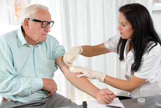 A photo of a nurse drawing blood from an older man at a doctor’s office.