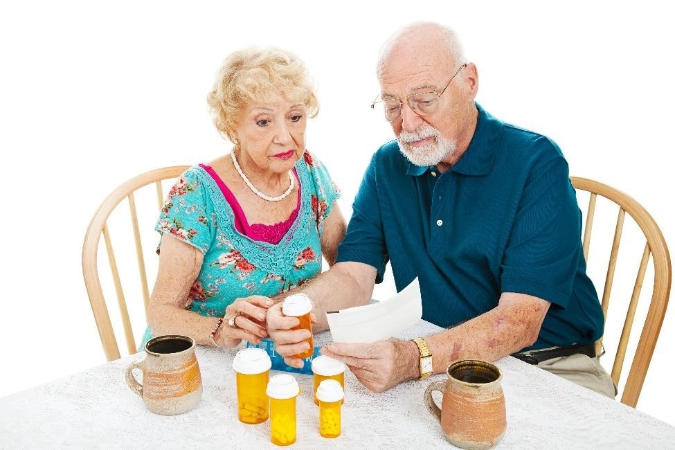 Older adult couple sitting at a table, looking at medicine bottles and receipts.