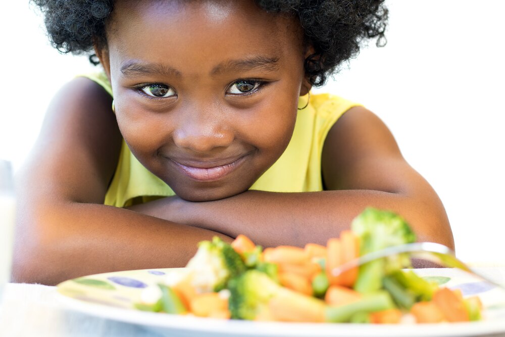Young girl smiling over a plate of vegetables.