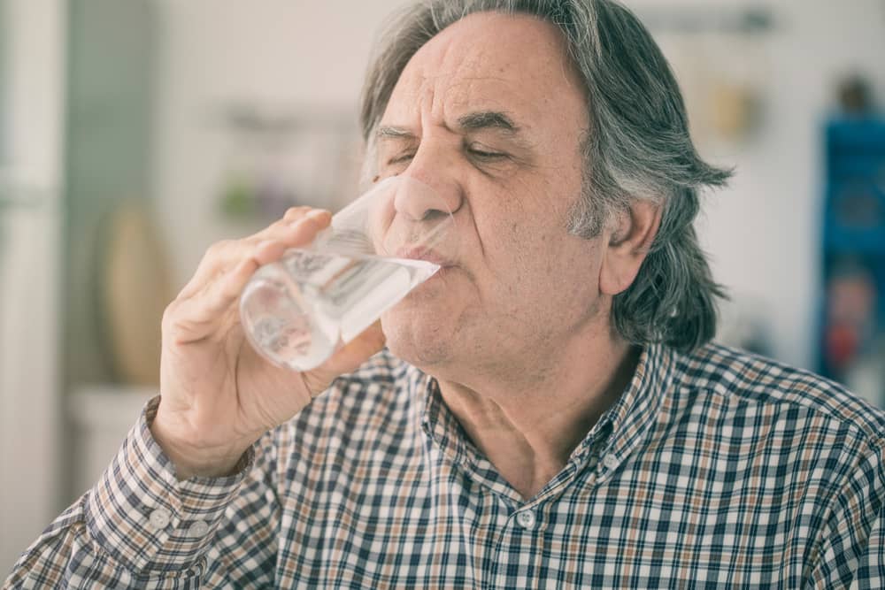 An older man drinks a tall glass of water.