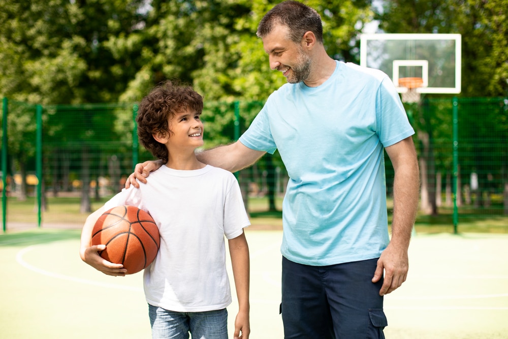 Un padre y un hijo sonrientes en la cancha de baloncesto de un parque.