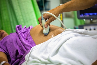 Photo of a pregnant woman getting a sonogram of her abdomen from a health care provider.