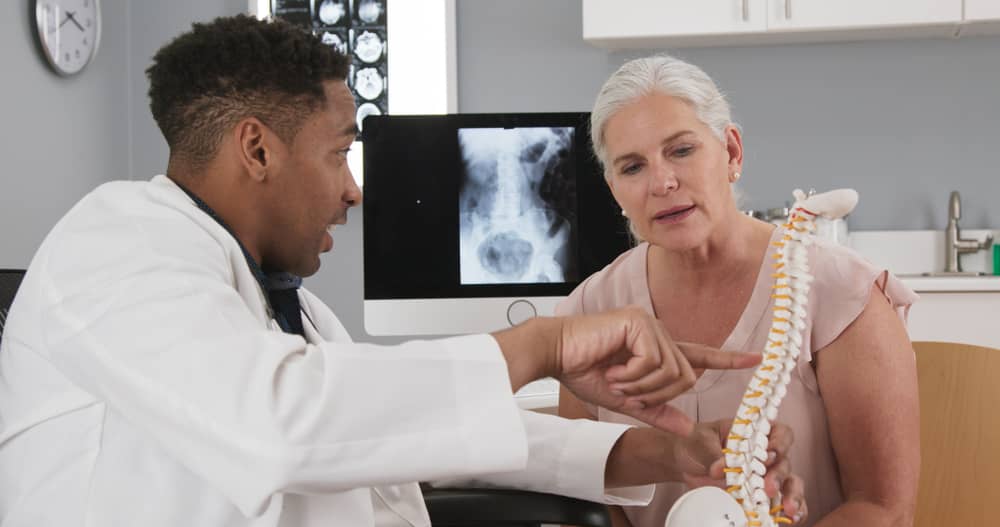 Un profesional del cuidado de la salud muestra una maqueta de la columna vertebral a una mujer.