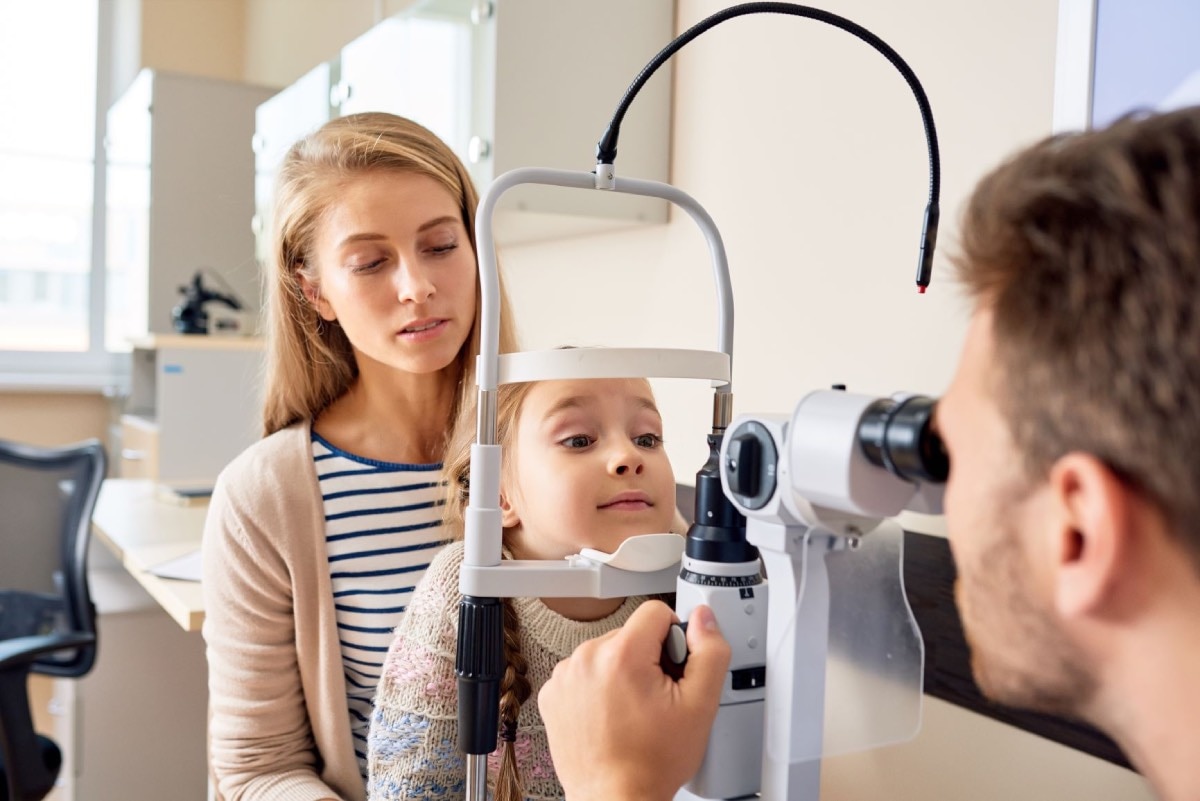 A child sitting in her mother’s lap while a doctor uses a slit-lamp to examine the child’s eyes