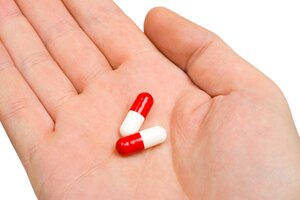 An open hand holding two medicine capsules.