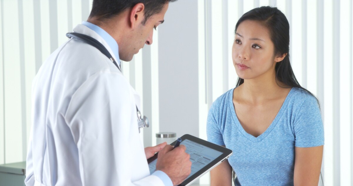 A health care professional taking a medical history from a young Asian woman.