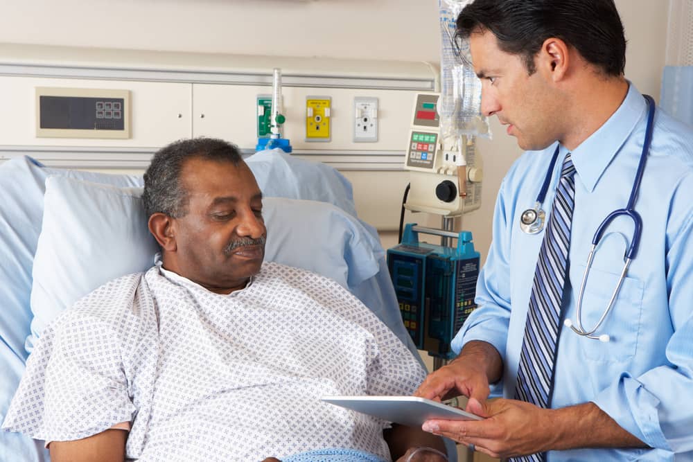 Doctor talking with an older patient who is lying in a hospital bed.