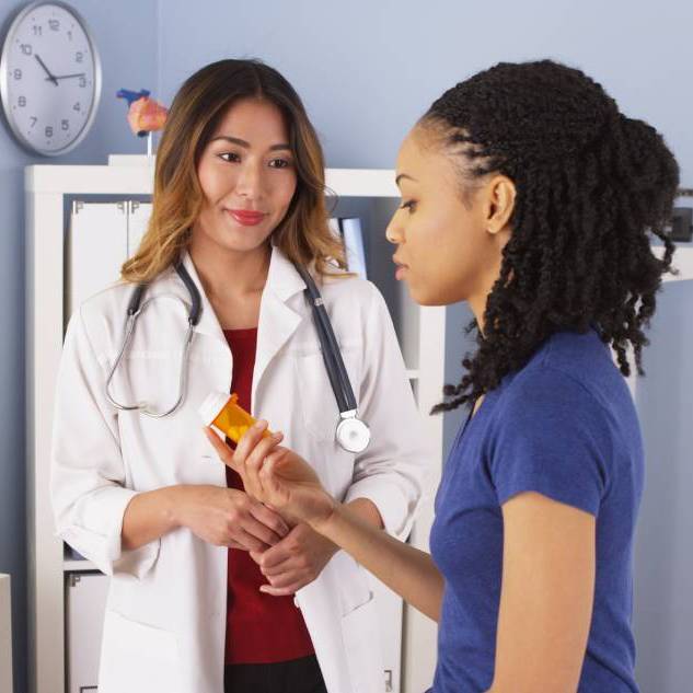 Doctora habla con una paciente que sostiene un frasco de medicamento.