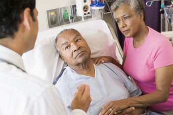 Un hombre mayor en una cama de hospital con su esposa y médico a su lado.