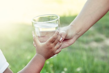 A child taking a glass of water from an adult.