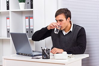 Man drinks from a large glass of water as he works on a computer.