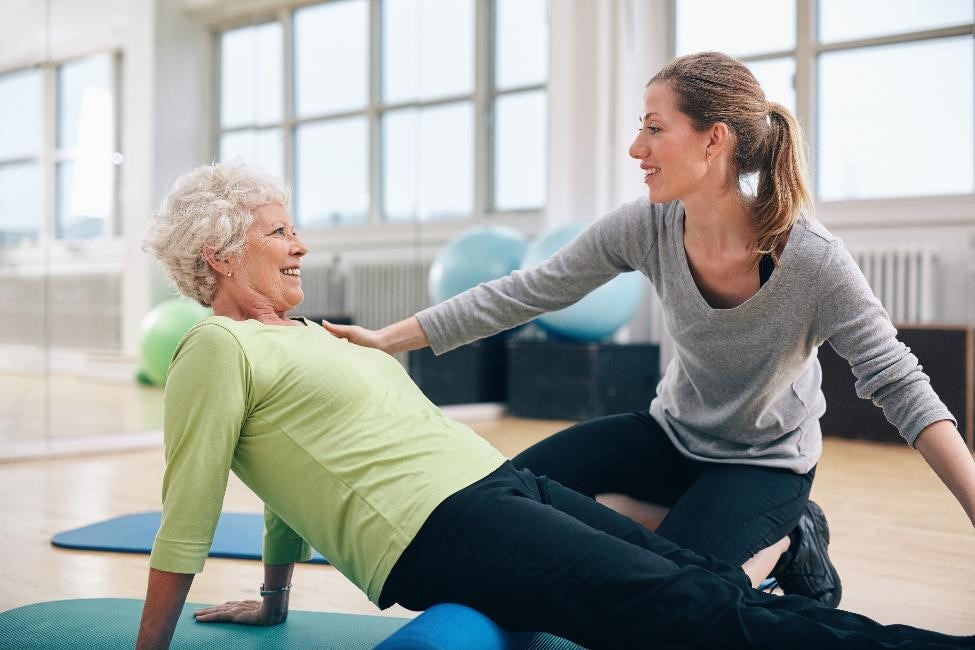 An older woman stretching while a physical therapist guides her.