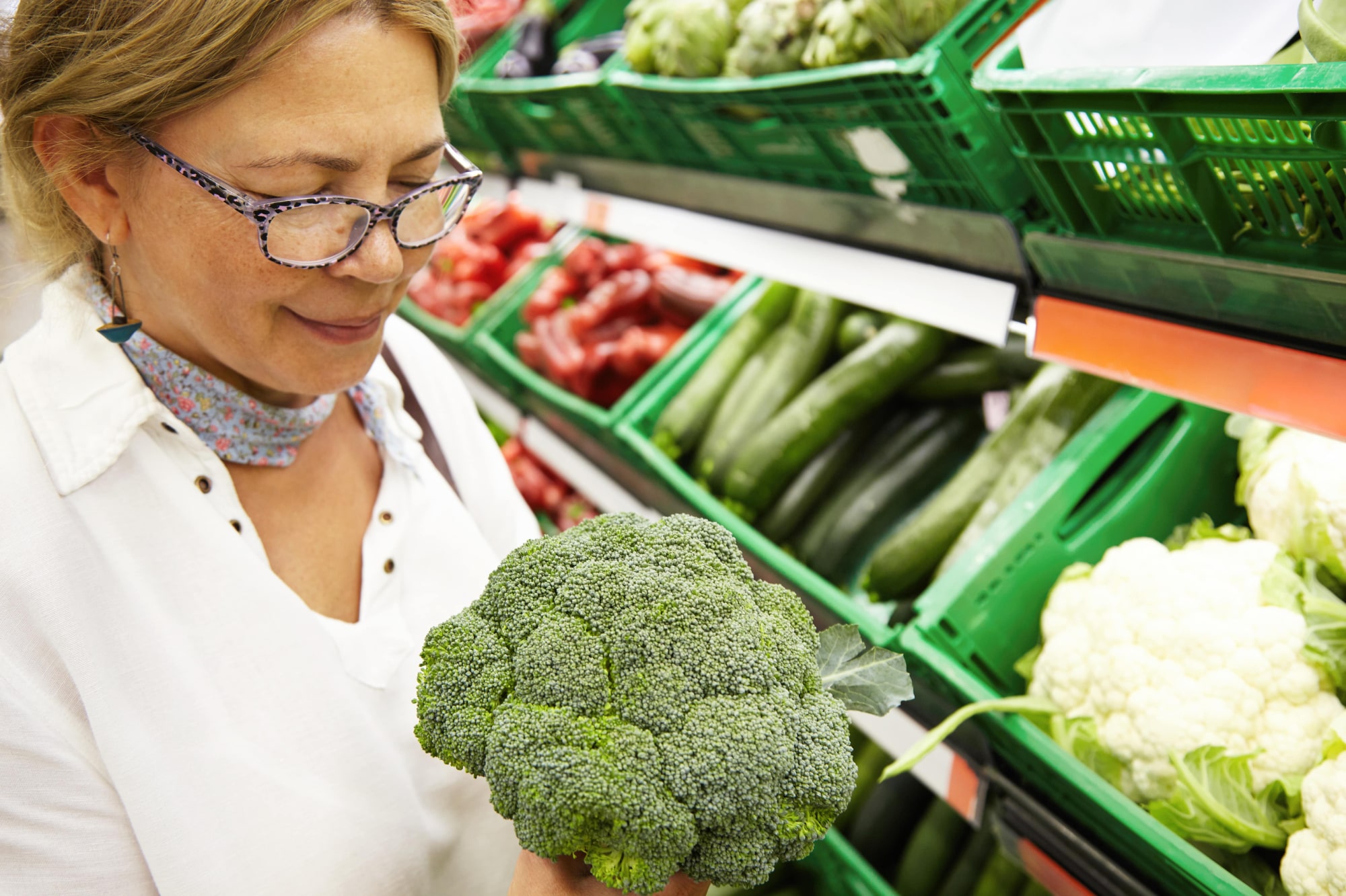 A woman shopping for broccoli in a grocery store.