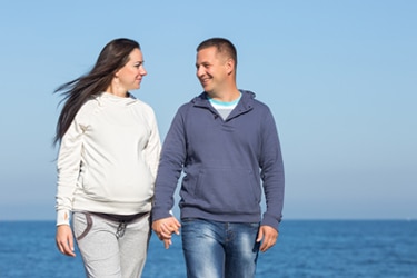 A pregnant woman and her male partner walking on a beach.