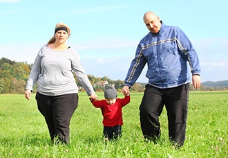 A man and woman who have overweight walk in a field with a young child.